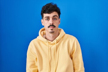 Fototapeta premium Hispanic man standing over blue background relaxed with serious expression on face. simple and natural looking at the camera.
