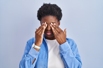 African american woman standing over blue background rubbing eyes for fatigue and headache, sleepy...