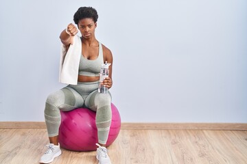 African american woman wearing sportswear sitting on pilates ball looking unhappy and angry showing...