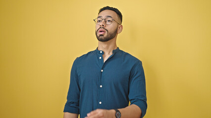 Young hispanic man with pollen allergy sneezing over isolated yellow background