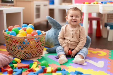 Adorable toddler playing with wooden construction blocks sitting on floor at kindergarten - obrazy, fototapety, plakaty