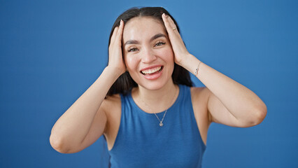 Young beautiful hispanic woman laughing a lot standing with hands on head over isolated blue...