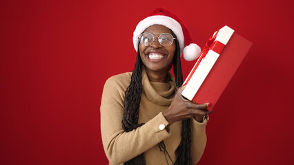 African woman smiling confident holding christmas gift over isolated red background
