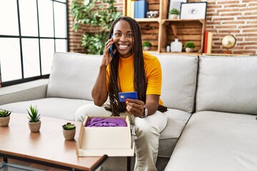 Obraz premium African american woman talking on smartphone holding credit card for online purchase at home