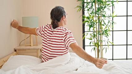 Middle age man waking up stretching arms at bedroom