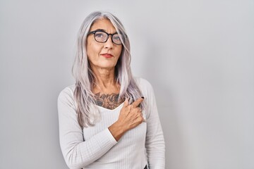 Middle age woman with grey hair standing over white background cheerful with a smile on face pointing with hand and finger up to the side with happy and natural expression