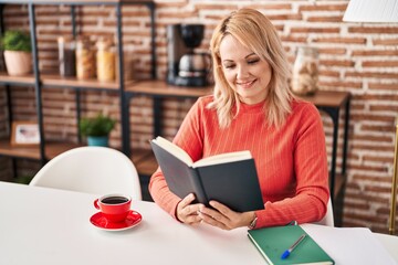 Young blonde woman reading book and drinking coffee at home