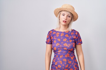 Young caucasian woman wearing flowers dress and summer hat looking sleepy and tired, exhausted for fatigue and hangover, lazy eyes in the morning.