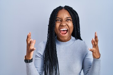 African american woman standing over blue background crazy and mad shouting and yelling with...