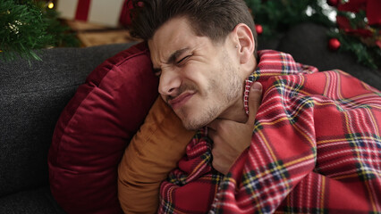 Obraz premium Young hispanic man suffering for throat pain lying on sofa by christmas tree at home