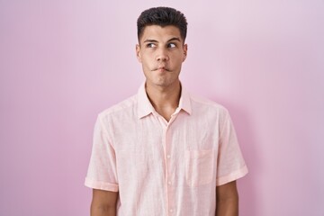 Young hispanic man standing over pink background making fish face with lips, crazy and comical gesture. funny expression.