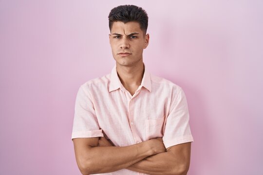Young hispanic man standing over pink background skeptic and nervous, disapproving expression on face with crossed arms. negative person.