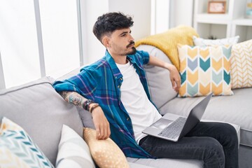 Young hispanic man using laptop sitting on sofa at home