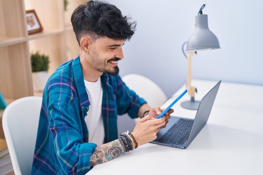 Young hispanic man using laptop and touchpad sitting on table at home
