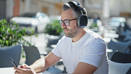 Grey-haired man listening to music sitting on table at coffee shop terrace