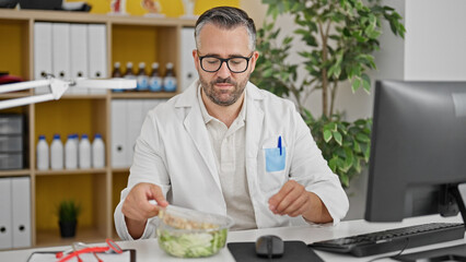 Grey-haired man doctor eating salad while work at the clinic