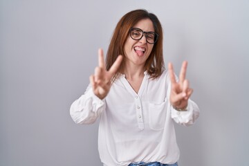 Brunette woman standing over white isolated background smiling with tongue out showing fingers of...
