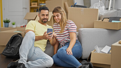 Fototapeta na wymiar Man and woman couple sitting on floor using smartphone smiling at new home