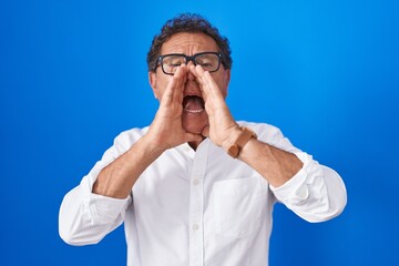 Naklejka premium Middle age hispanic man standing over blue background shouting angry out loud with hands over mouth