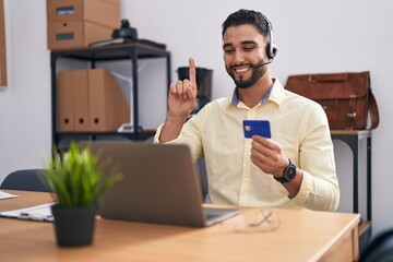 Hispanic young man wearing call center agent headset doing online shopping smiling with an idea or...