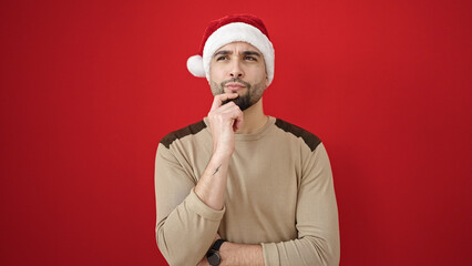 Young arab man wearing christmas hat with doubt expression over isolated red background