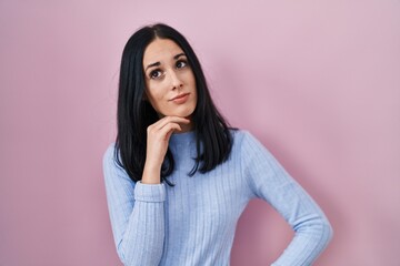 Obraz premium Hispanic woman standing over pink background with hand on chin thinking about question, pensive expression. smiling with thoughtful face. doubt concept.