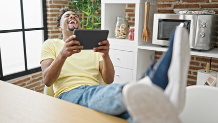 African american man watching video on touchpad laughing a lot at dinning room - obrazy, fototapety, plakaty