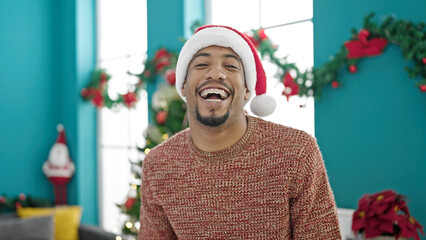 African american man wearing christmas hat laughing a lot at home