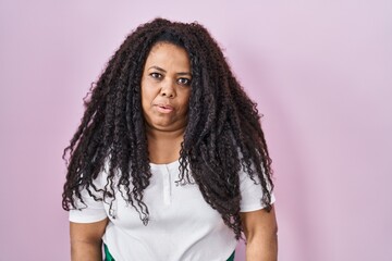 Plus size hispanic woman standing over pink background looking sleepy and tired, exhausted for fatigue and hangover, lazy eyes in the morning.