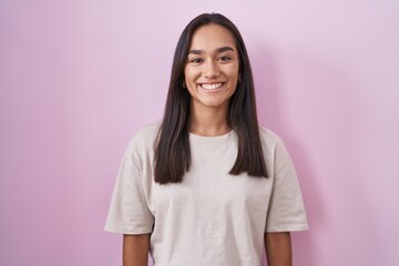 Young hispanic woman standing over pink background with a happy and cool smile on face. lucky...