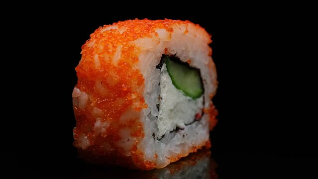 California sushi roll rotating on black background on mirrored table close-up. Fresh roll with crab, cream cheese, cucumber, rice topped with orange tobiko caviar. 