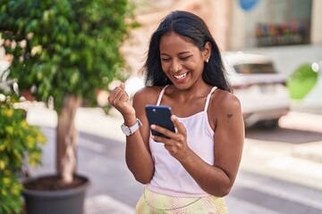 Young beautiful woman using smartphone with winner expression at street