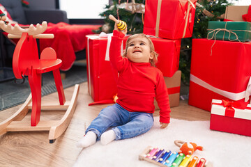 Adorable hispanic toddler holding maraca sitting on floor by christmas tree at home