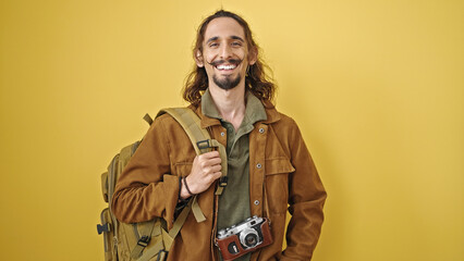 Young hispanic man tourist wearing backpack smiling over isolated yellow background