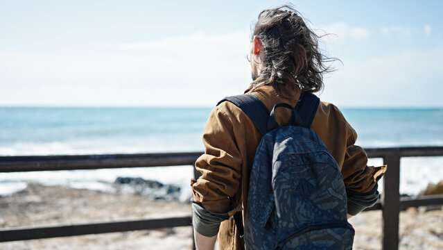 Young hispanic man tourist wearing backpack standing backwards at seaside