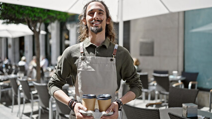 Young hispanic man waiter smiling confident holding take away coffee at coffee shop terrace