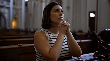 Young beautiful hispanic woman praying on a church bench at Augustinian Church in Vienna