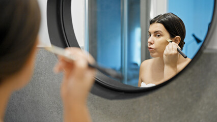 Young beautiful hispanic woman applying make up in the bathroom