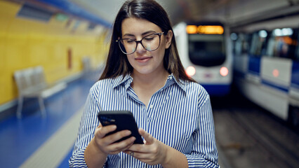 Young beautiful hispanic woman waiting for the subway using smartphone in subway station of Madrid