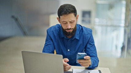 Fototapeta premium Young hispanic man business worker using laptop and smartphone at the office