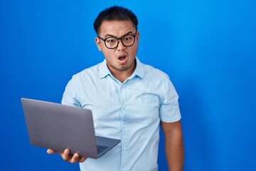 Chinese young man using computer laptop in shock face, looking skeptical and sarcastic, surprised...