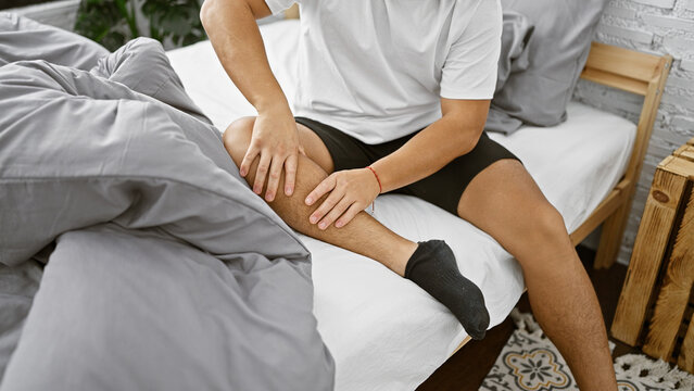 Awake early in the morning, a young chinese man suffers from agonizing leg pain in his home bedroom, anxiously massaging his injured limb