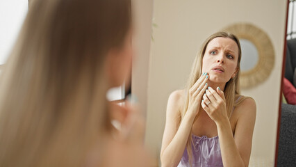 Young blonde woman looking face on mirror with upset expression at street