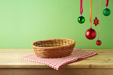 Empty basket on wooden table with hanging ornament decoration and tablecloth over green background....