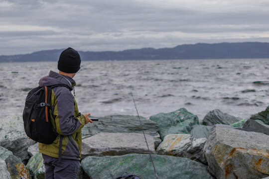 A man fishing from the shore of a fjord in Norway.