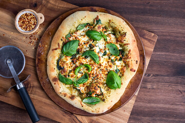 A homemade pesto and greens gourmet pizza garnished with basil and chilis.