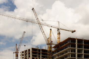 Tower cranes work during the construction of a multi-story building. New apartments for residents and premises for offices. Risky work at height. Lifting heavy building materials. City development