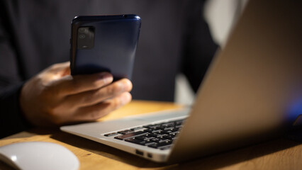 Hands using a smartphone and laptop simultaneously for secure login, highlighting the importance of multi-factor authentication.