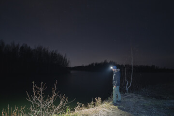 A man with a headlamp at night in nature near a river, photo with low lighting.