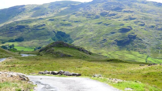Narrow winding mountain road down to Duddon valley in Cumbrian mountains, Hardknott Pass, Hard Knott Pass viewpoint panning shot.